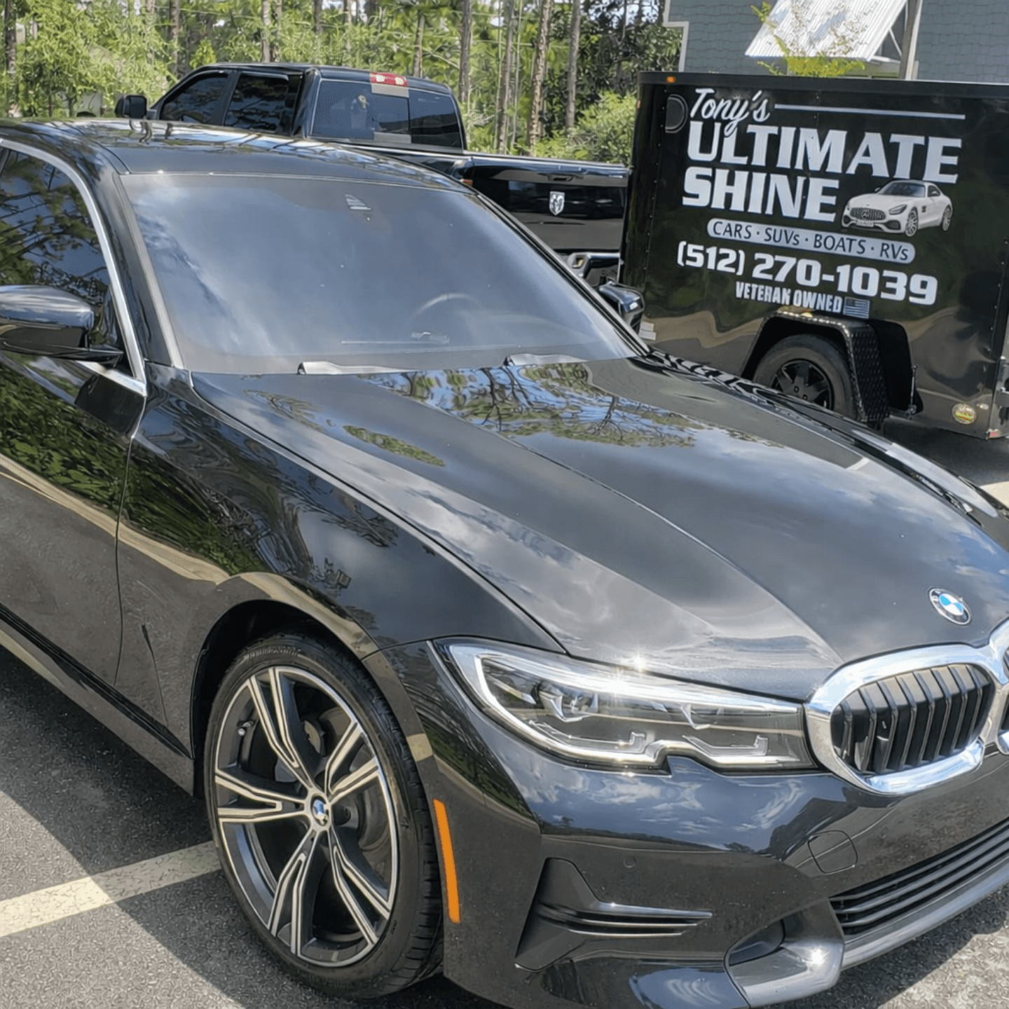 Glossy black BMW sedan freshly detailed with mobile detailing trailer in background